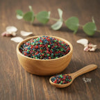 Coupelle en bois remplie de grains d’encens Saint Jean Baptiste multicolores avec petite cuillère sur table en bois.
