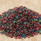 Gros plan sur des grains d’encens Saint Jean Baptiste rouges, bleus et verts sur fond clair.
