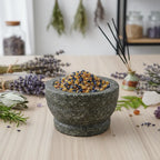 Grains d'encens de résine Saint Joseph (bleu et ocre) présentés dans un mortier en granit gris, sur une table décorée d'herbes séchées et de lavande.
