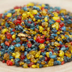 Gros plan sur des grains d’encens Saint Jude multicolores rouges, jaunes, bleus et noirs sur fond clair.
