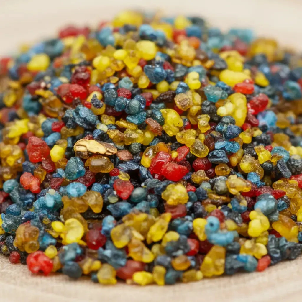 Gros plan sur des grains d’encens Saint Jude multicolores rouges, jaunes, bleus et noirs sur fond clair.
