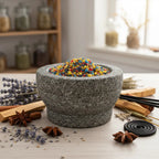 Mortier en pierre rempli de grains d’encens Saint Jude multicolores, entouré de lavande, bâtonnets d’encens et étoiles d’anis sur table en bois claire.
