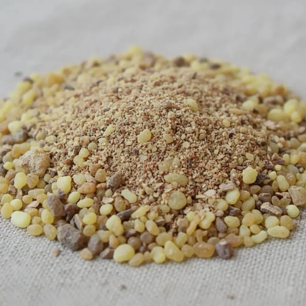 Gros plan sur un monticule de grains d'encens de résine Saint Michel, montrant des morceaux de résine jaune ambrée recouverts d'une poudre brun-beige, sur un fond en tissu clair.