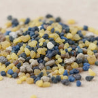 Gros plan sur des grains d’encens Saint Paul jaunes, bleus et bruns sur fond clair.