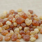 Gros plan sur des grains d’encens Saint Uriel aux teintes ambrées et dorées sur fond clair.
