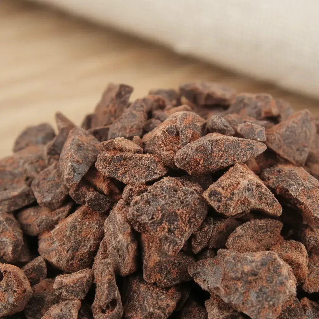 Gros plan sur un monticule de morceaux de résine Sang de Dragon, montrant leur couleur brun-rouge foncé, irrégulière et terreuse, avec une texture granuleuse.