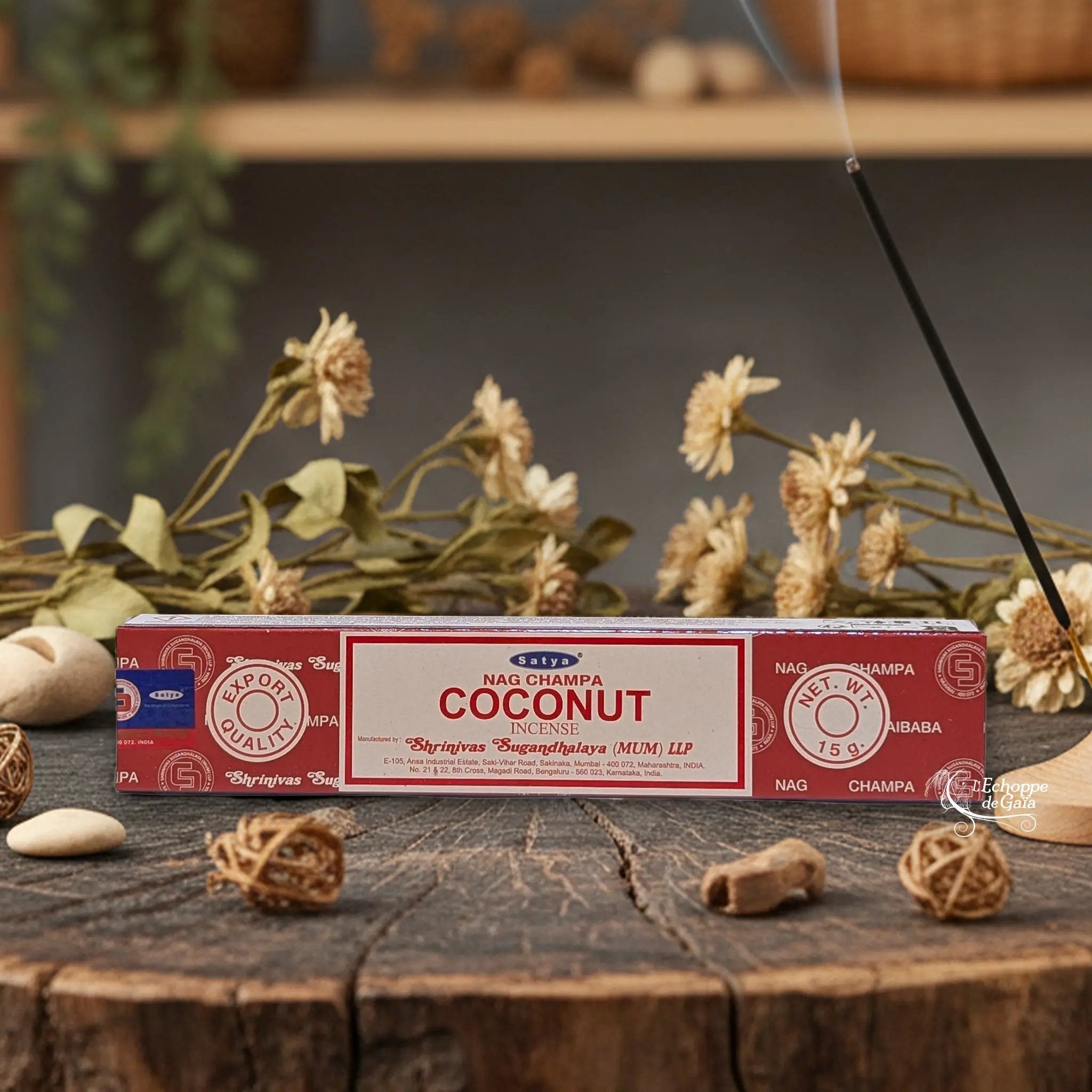 Boîte d'encens Satya Nag Champa "Coconut" posée sur une table en bois avec des fleurs séchées et un bâton d'encens fumant.