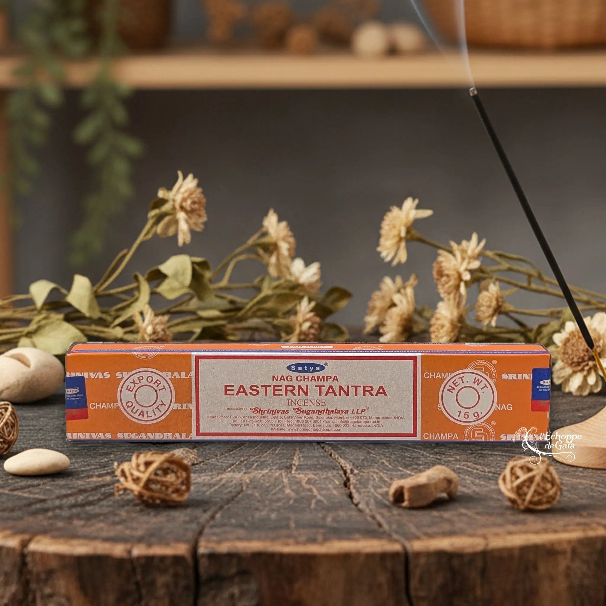 Boîte d'encens Satya Nag Champa "Eastern Tantra" posée sur une table en bois avec des fleurs séchées et un bâton d'encens fumant.
