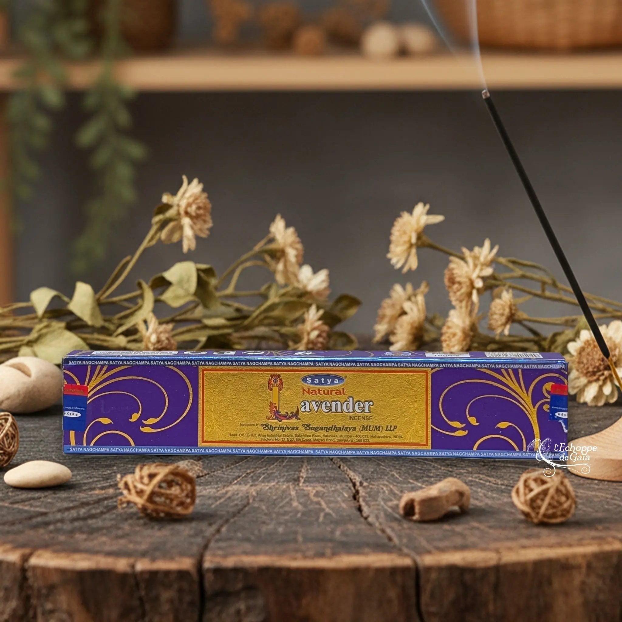 Boîte d'encens Satya "Natural Lavender" posée sur une table en bois avec des fleurs séchées et un bâton d'encens fumant.