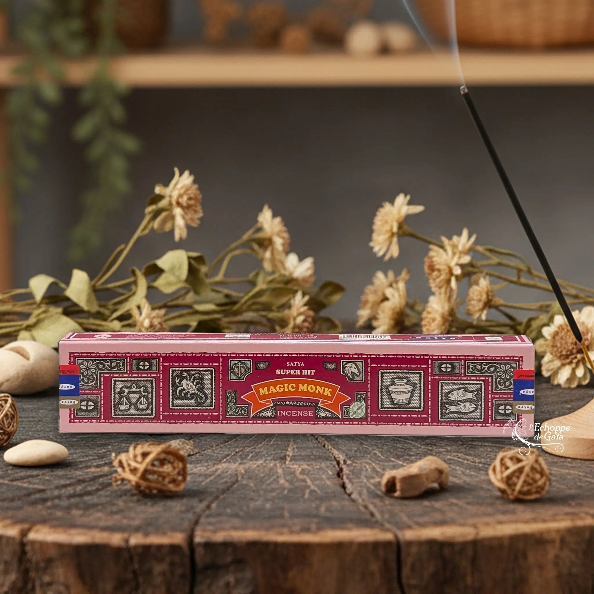Boîte d'encens Satya Super Hit "Magic Monk" posée sur une table en bois avec des fleurs séchées et un bâton d'encens fumant.
