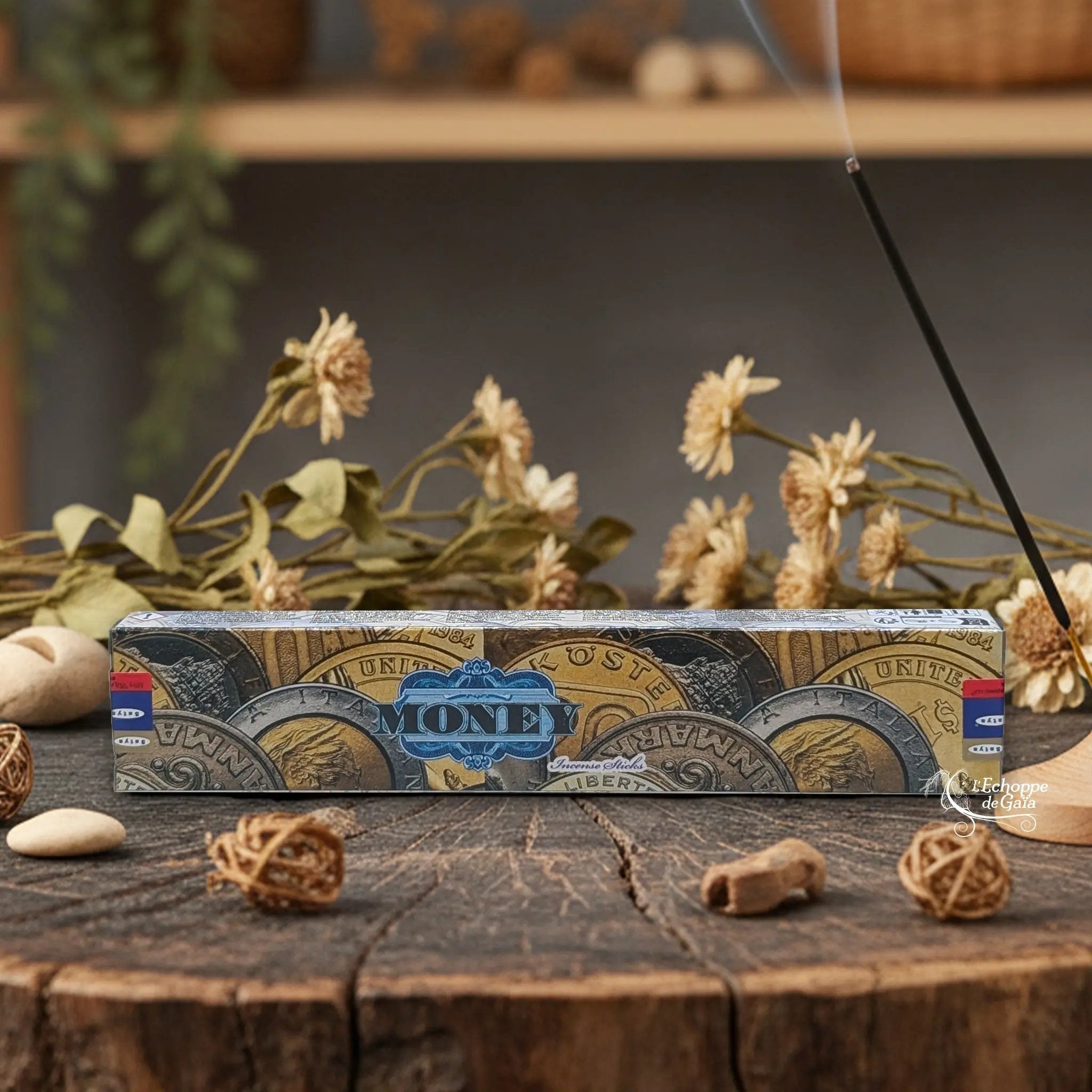 Boîte d'encens Satya "Money" posée sur une table en bois avec des fleurs séchées et un bâton d'encens fumant.