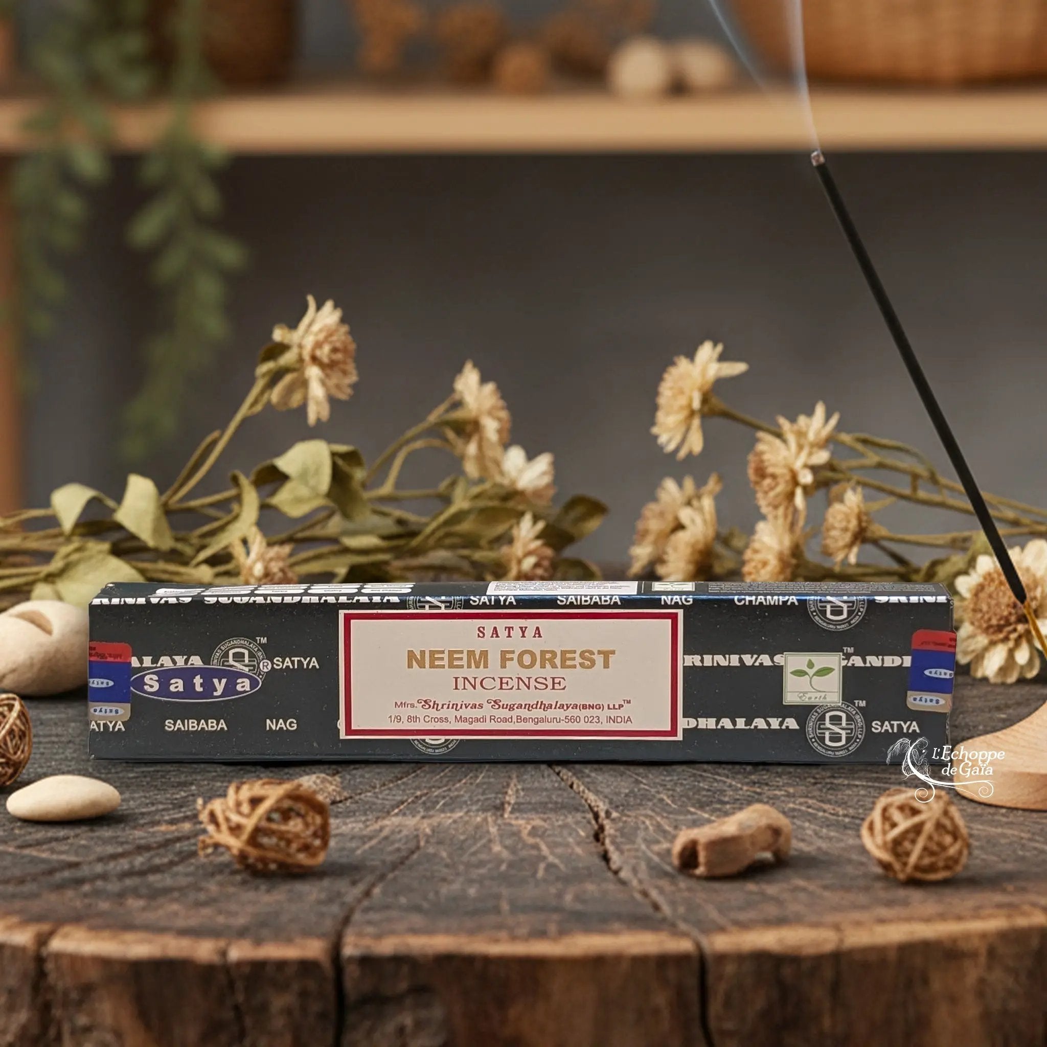 Boîte d'encens Satya "Neem Forest" posée sur une table en bois avec des fleurs séchées et un bâton d'encens fumant.