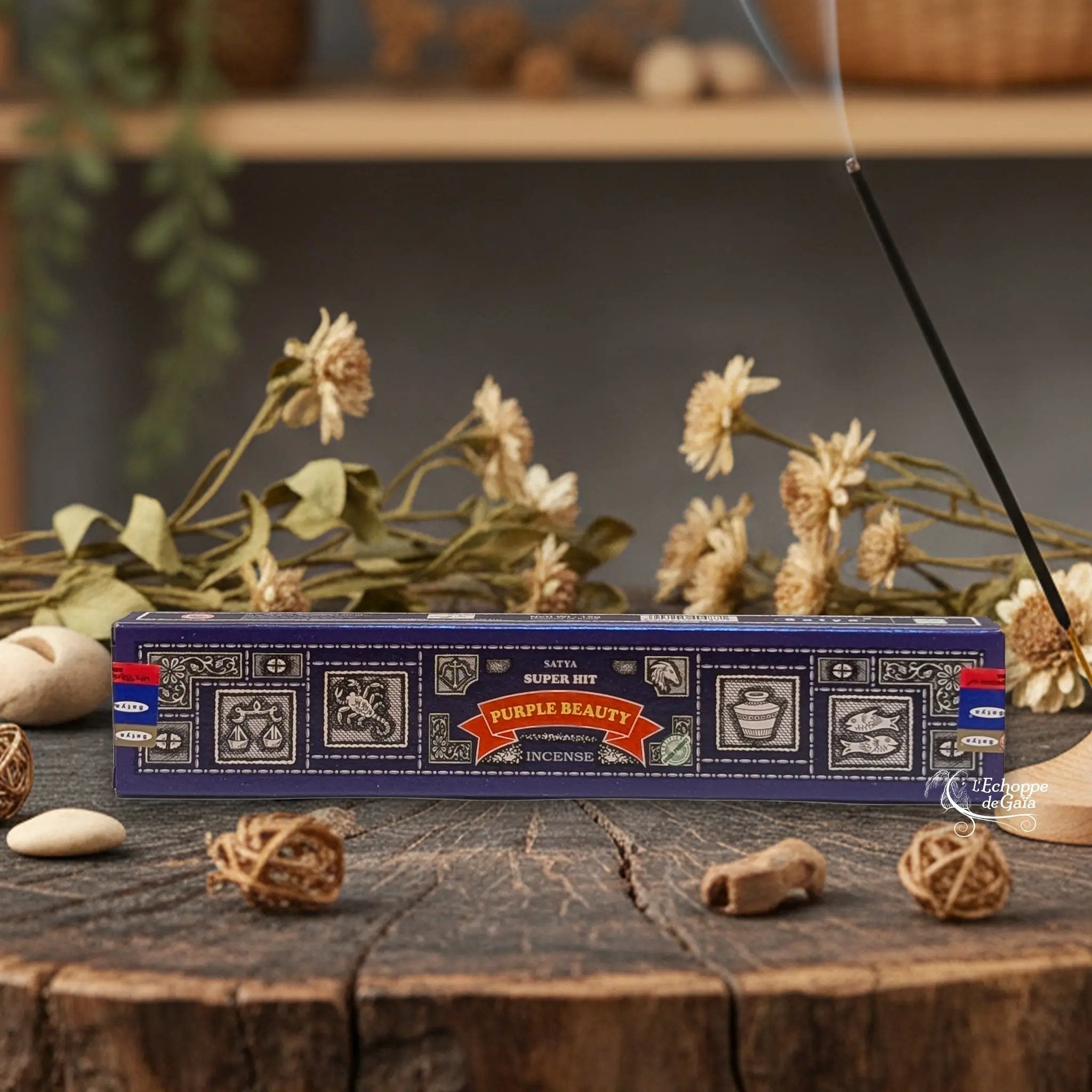 Boîte d'encens Satya Super Hit "Purple Beauty" posée sur une table en bois avec des fleurs séchées et un bâton d'encens fumant.
