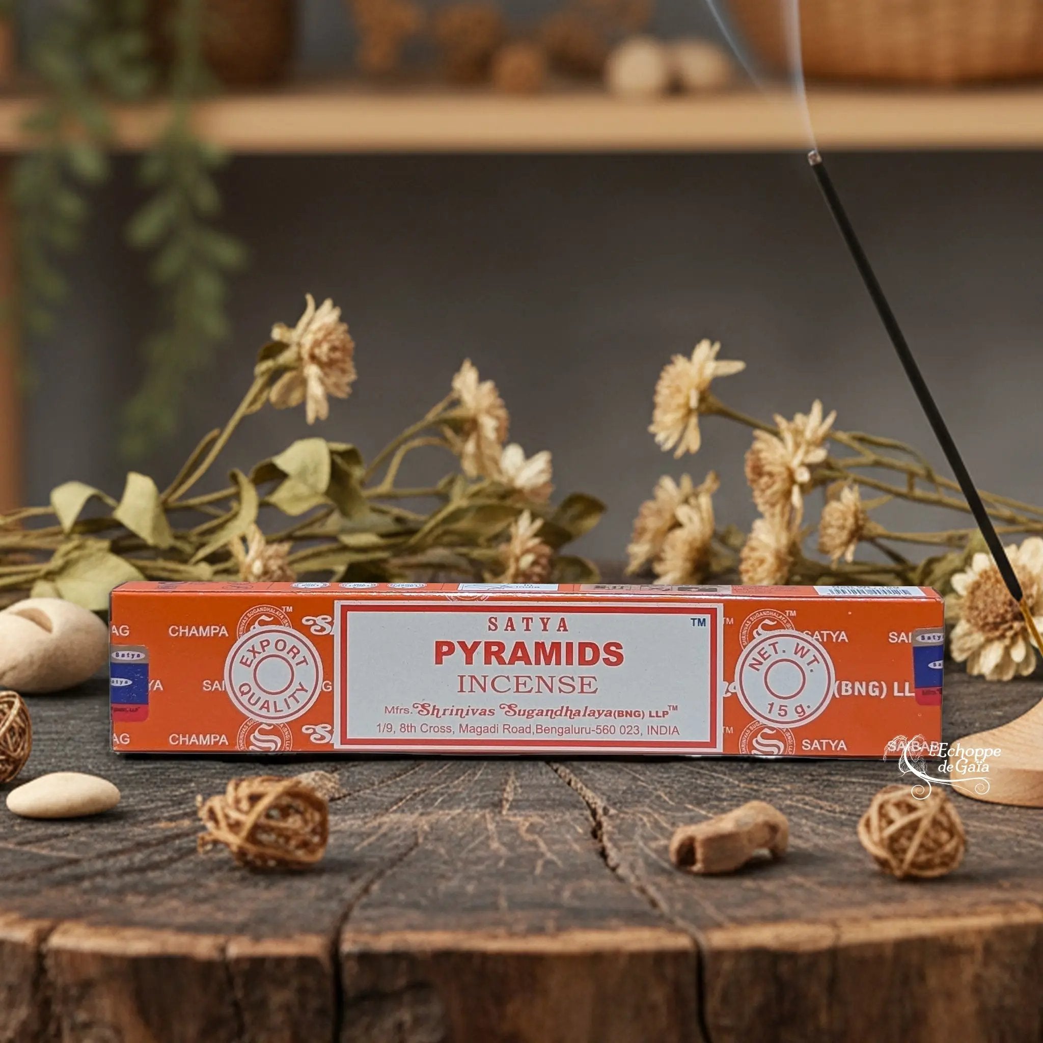 Boîte d'encens Satya "Pyramids" posée sur une table en bois avec des fleurs séchées et un bâton d'encens fumant.