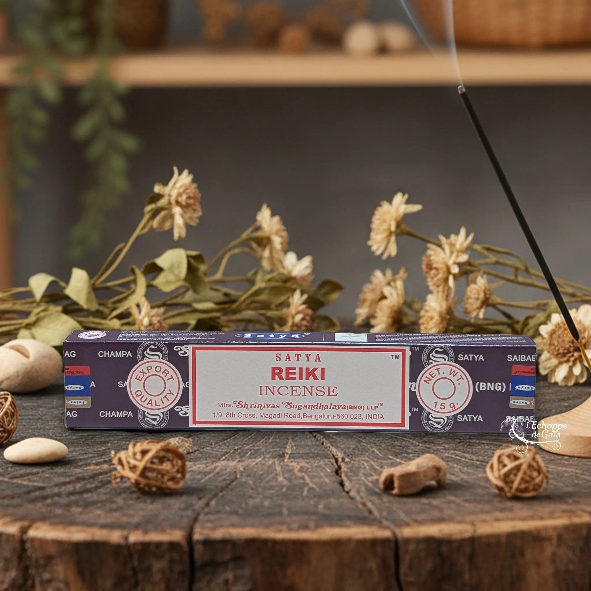 Boîte d'encens Satya "Reiki" posée sur une table en bois avec des fleurs séchées et un bâton d'encens fumant.