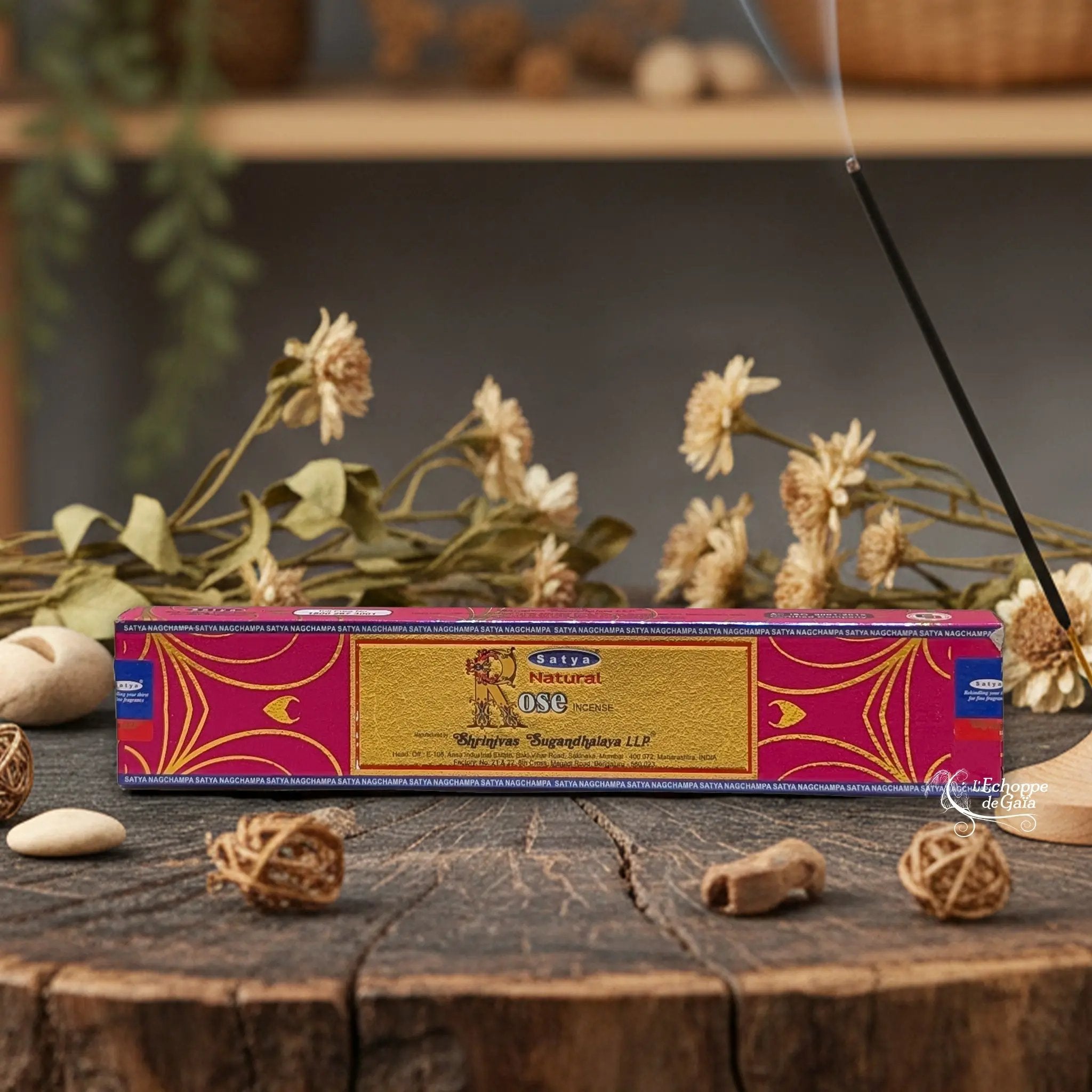 Boîte d'encens Satya "Natural Rose" posée sur une table en bois avec des fleurs séchées et un bâton d'encens fumant.