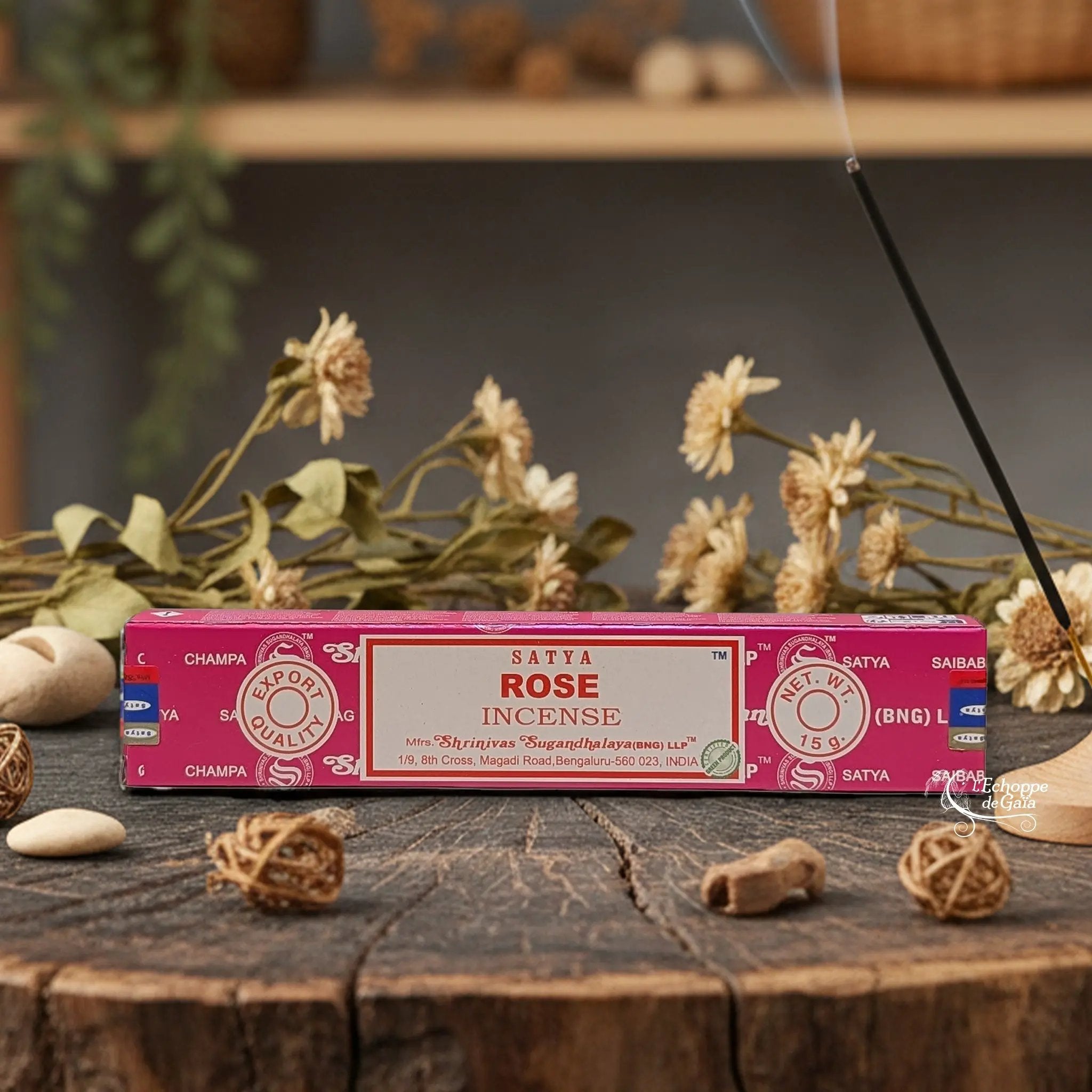 Boîte d'encens Satya "Rose" posée sur une table en bois avec des fleurs séchées et un bâton d'encens fumant.