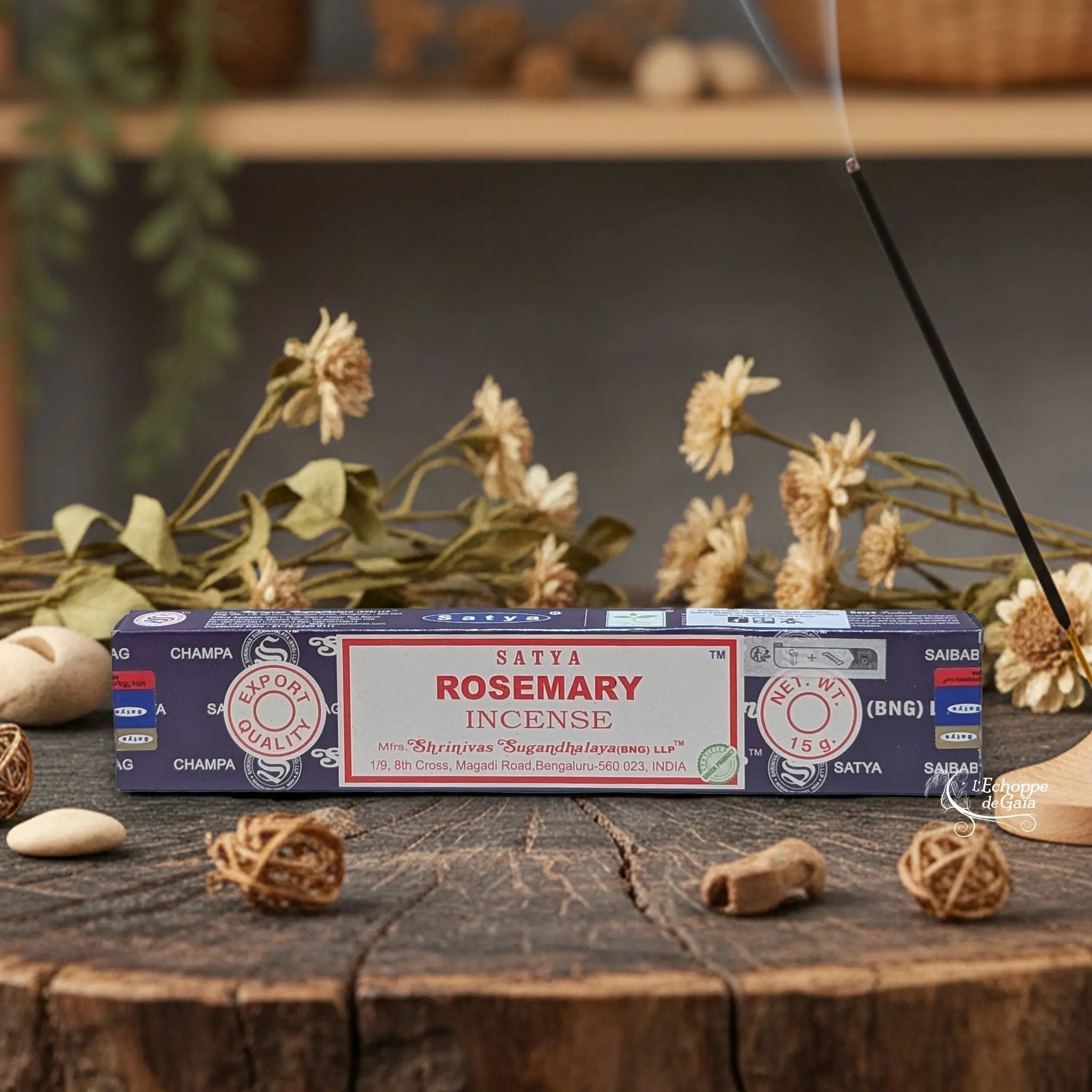 Boîte d'encens Satya "Rosemary" posée sur une table en bois avec des fleurs séchées et un bâton d'encens fumant.