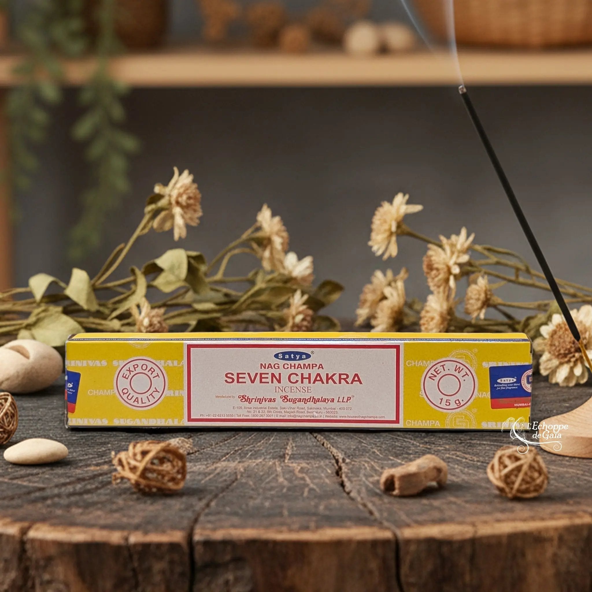 Boîte d'encens Satya Nag Champa "Seven Chakra" posée sur une table en bois avec des fleurs séchées et un bâton d'encens fumant.