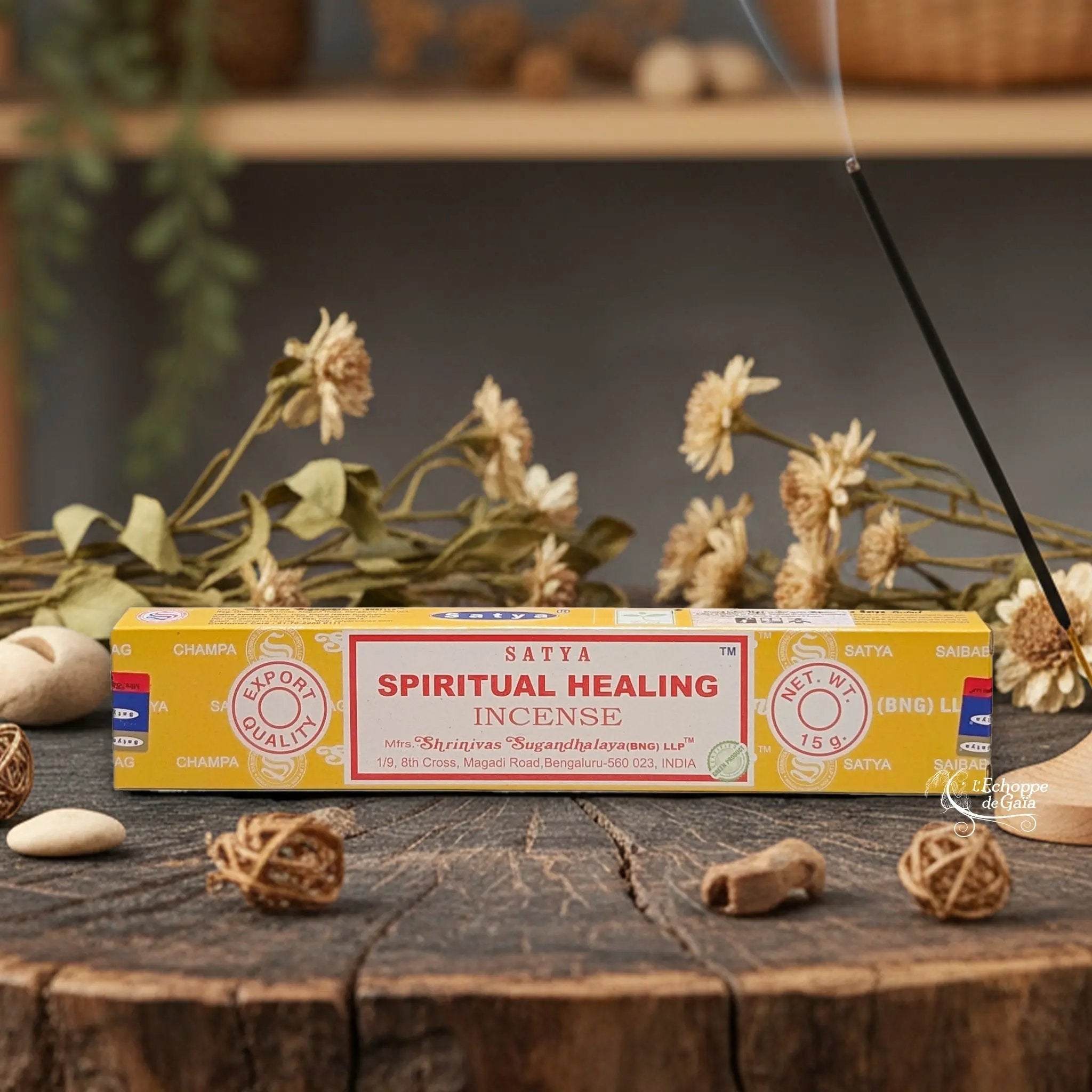 Boîte d'encens Satya "Spiritual Healing" posée sur une table en bois avec des fleurs séchées et un bâton d'encens fumant.