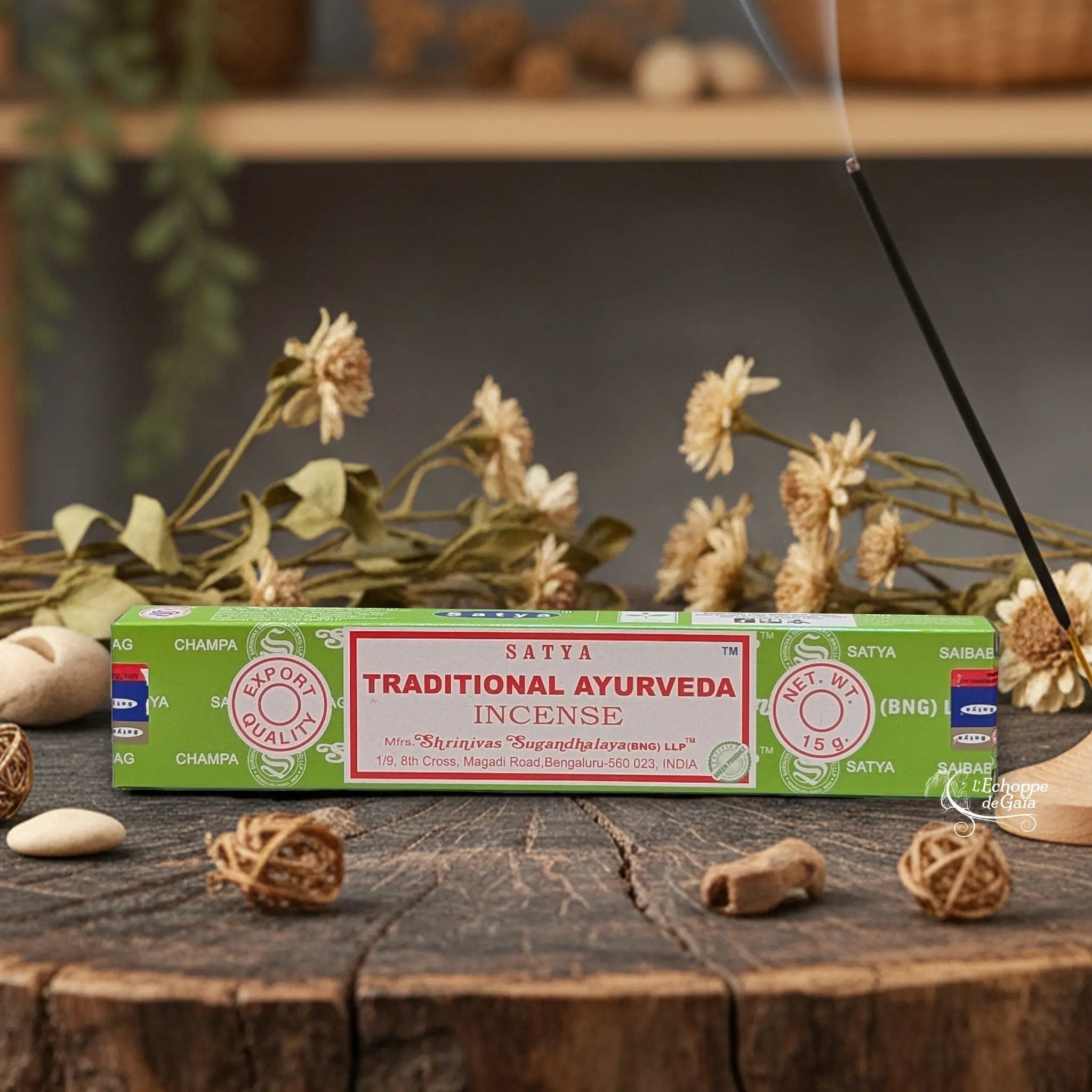 Boîte d'encens Satya "Traditional Ayurveda" posée sur une table en bois avec des fleurs séchées et un bâton d'encens fumant.