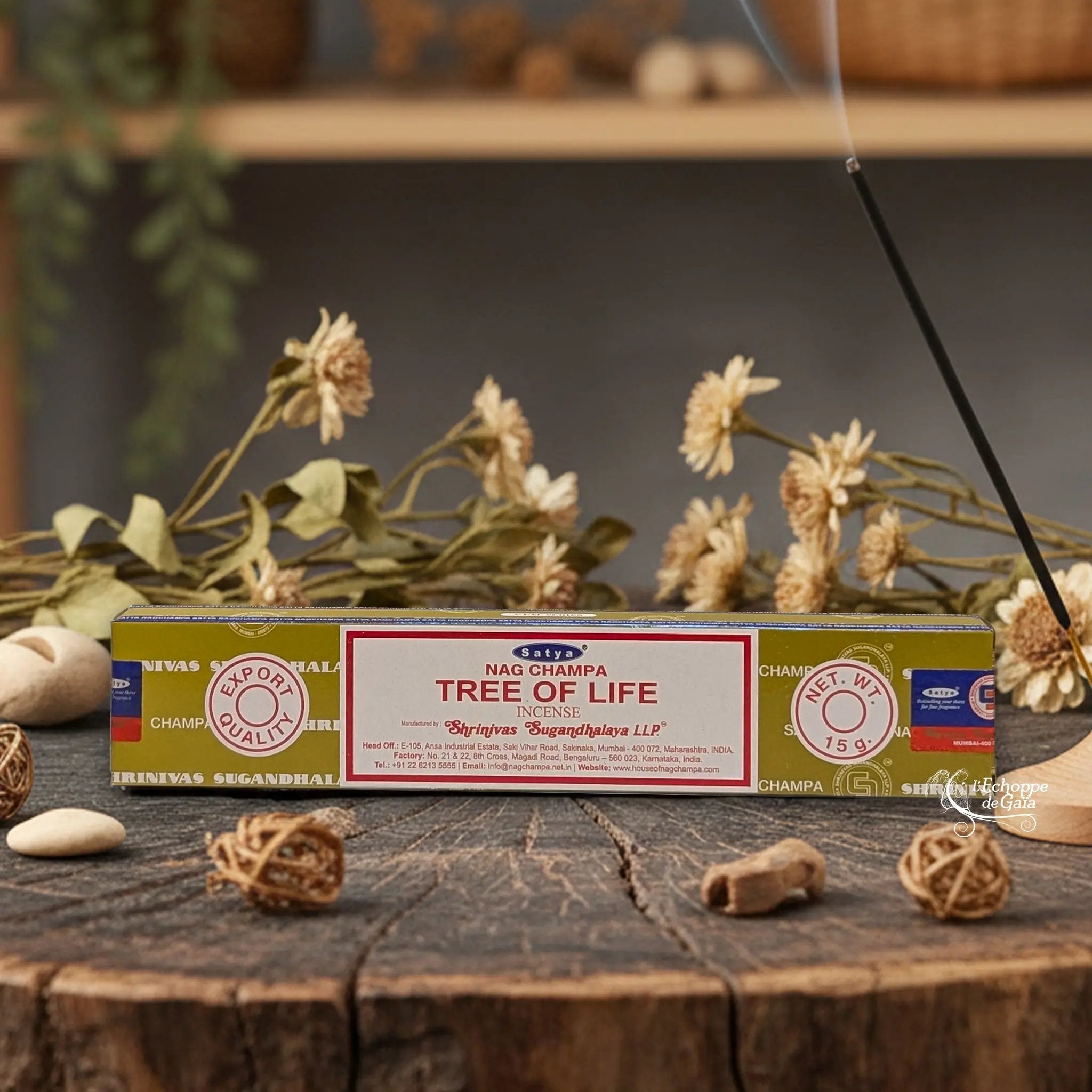 Boîte d'encens Satya Nag Champa "Tree of Life" posée sur une table en bois avec des fleurs séchées et un bâton d'encens fumant.