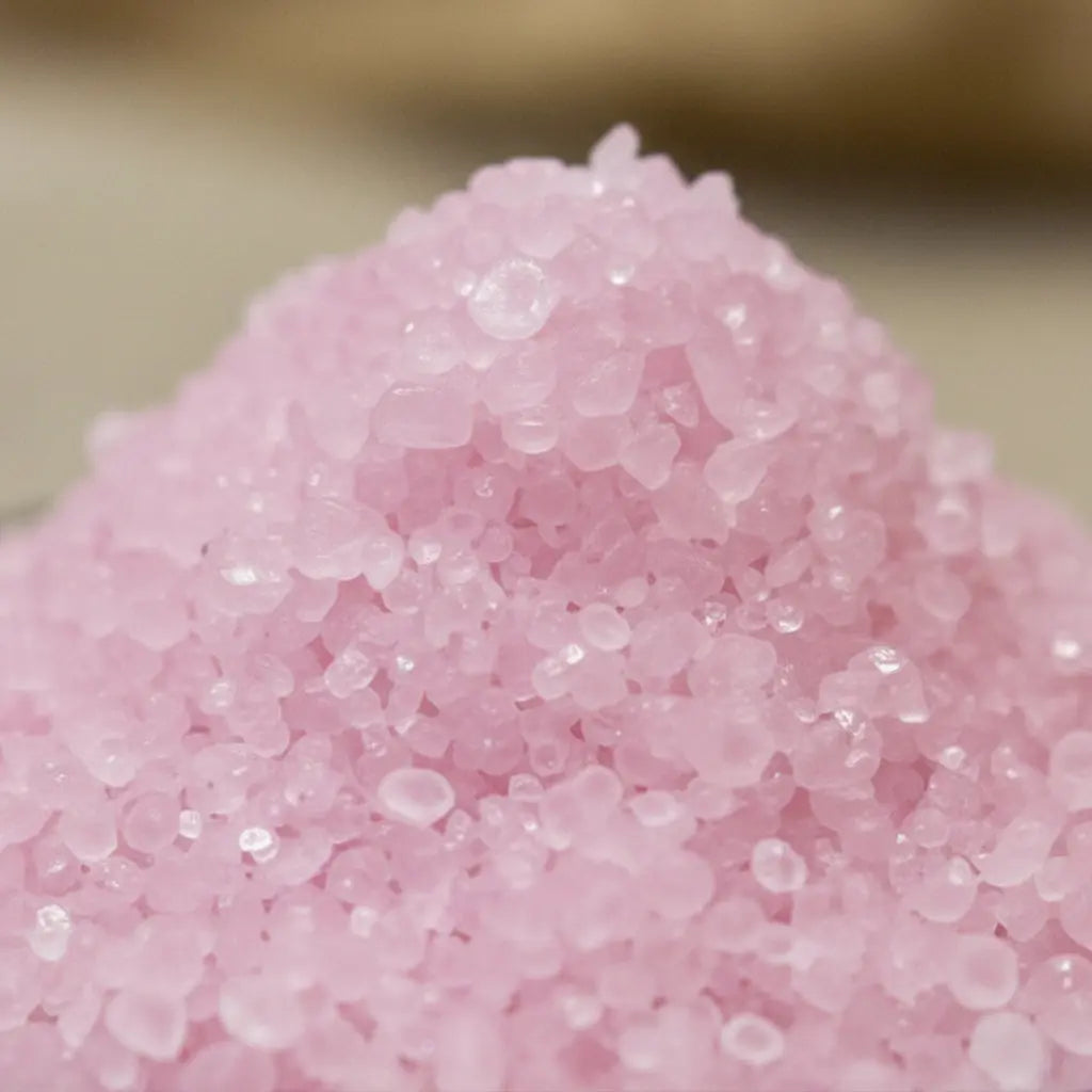 Gros plan sur des cristaux de sel infusé à la Rose de Minuit, texture cristalline rose pâle.