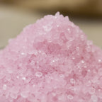 Gros plan sur des cristaux de sel infusé à la Rose de Minuit, texture cristalline rose pâle.