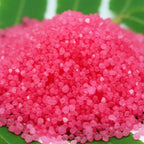 Gros plan sur des cristaux de sel infusé à la Rose et au Musc, texture cristalline rose vif.