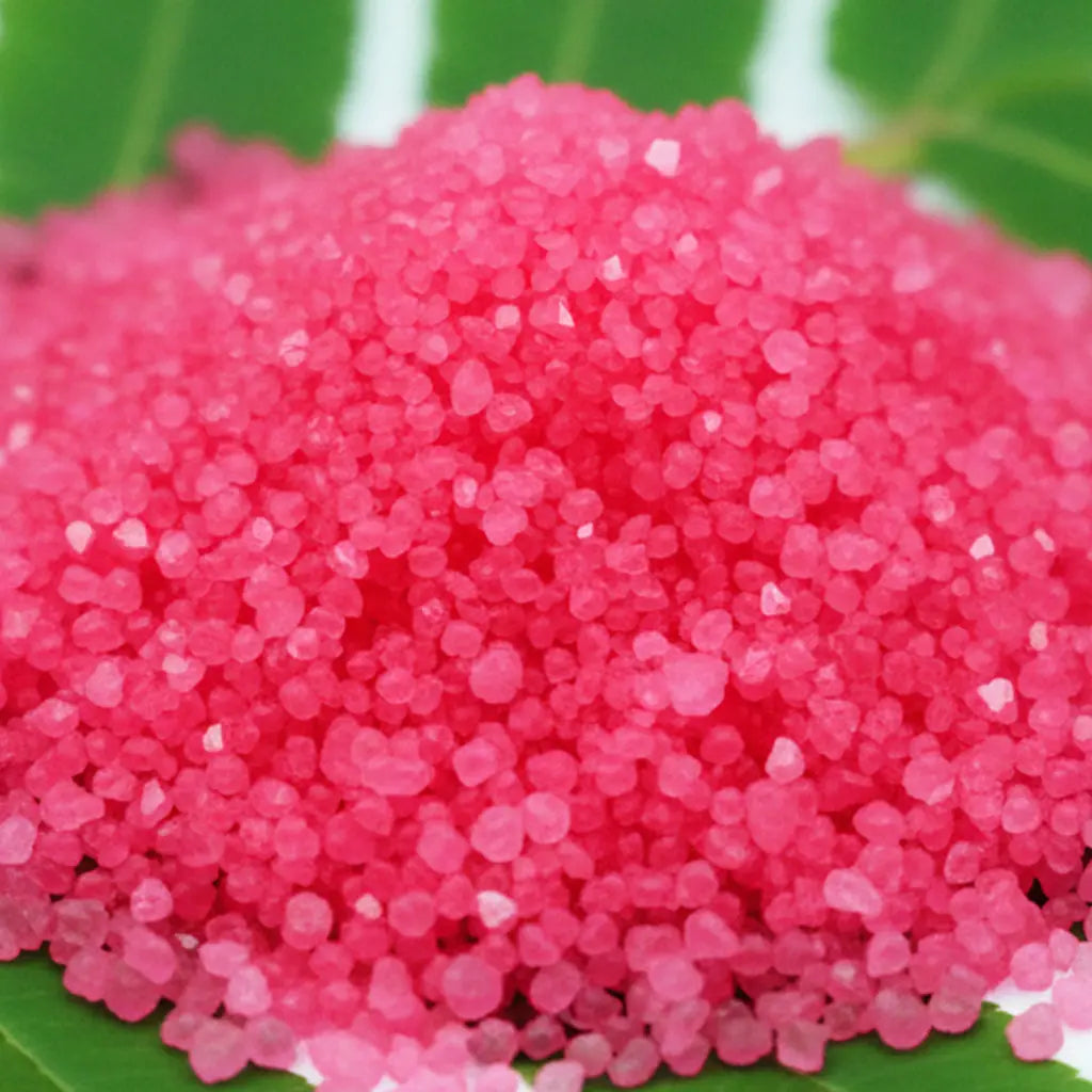 Gros plan sur des cristaux de sel infusé à la Rose et au Musc, texture cristalline rose vif.