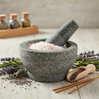 Grains de Sel Rose de l'Himalaya dans un mortier en granit gris avec pilon, entouré de brins de lavande, de romarin et de bâtonnets d'encens.