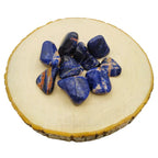 Un groupe de pierres de sodalite roulées d'un bleu profond marbré de blanc et d'orange, disposé sur une rondelle de bois clair.