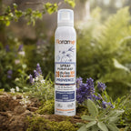 Flacon blanc de spray purifiant aux huiles essentielles bio, posé dans un jardin provençal parmi la lavande, la sauge et la mousse fraîche.
