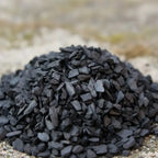 Gros plan sur des grains d’encens storax noirs en copeaux sur fond naturel.