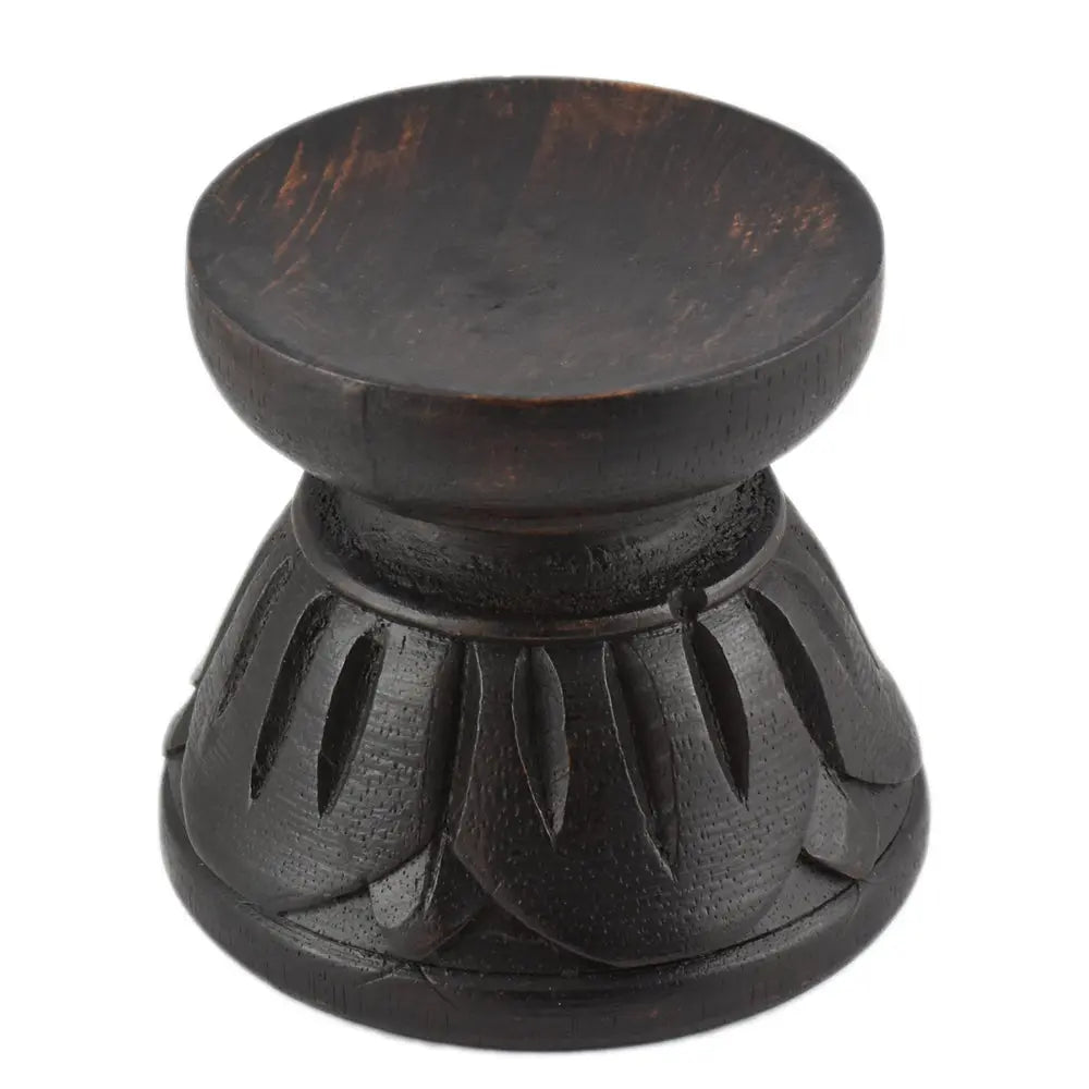 Support pour boule de cristal en bois sombre (noir/brun), forme de petit socle “lotus” : une base évasée sculptée de pétales arrondis tout autour, surmontée d’un col court et d’une coupelle circulaire plate en haut pour poser la boule. Finition mate, avec quelques nuances/brunissements visibles dans le bois. Photo détourée sur fond blanc.