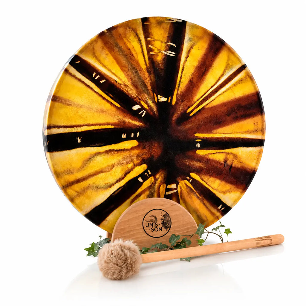 Tambour chamanique circulaire aux motifs rayonnants jaune et marron, posé sur un socle Unis-Son décoré de lierre avec sa mailloche, sur fond blanc.