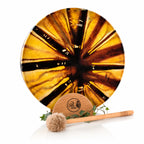 Tambour chamanique circulaire aux motifs rayonnants jaune et marron, posé sur un socle Unis-Son décoré de lierre avec sa mailloche, sur fond blanc.