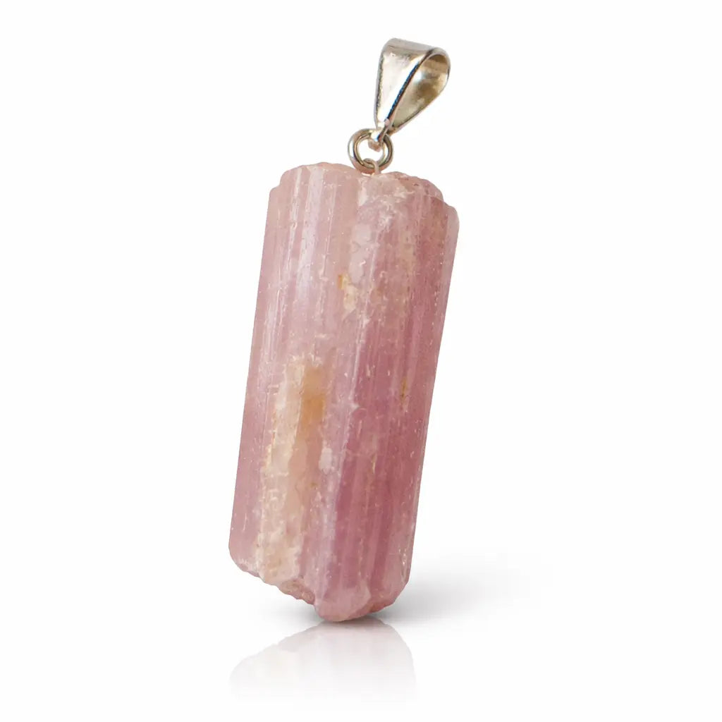 Un pendentif en tourmaline rose brute de forme cylindrique et striée, surmonté d'une bélière en métal argenté, présenté avec son reflet sur un fond blanc.