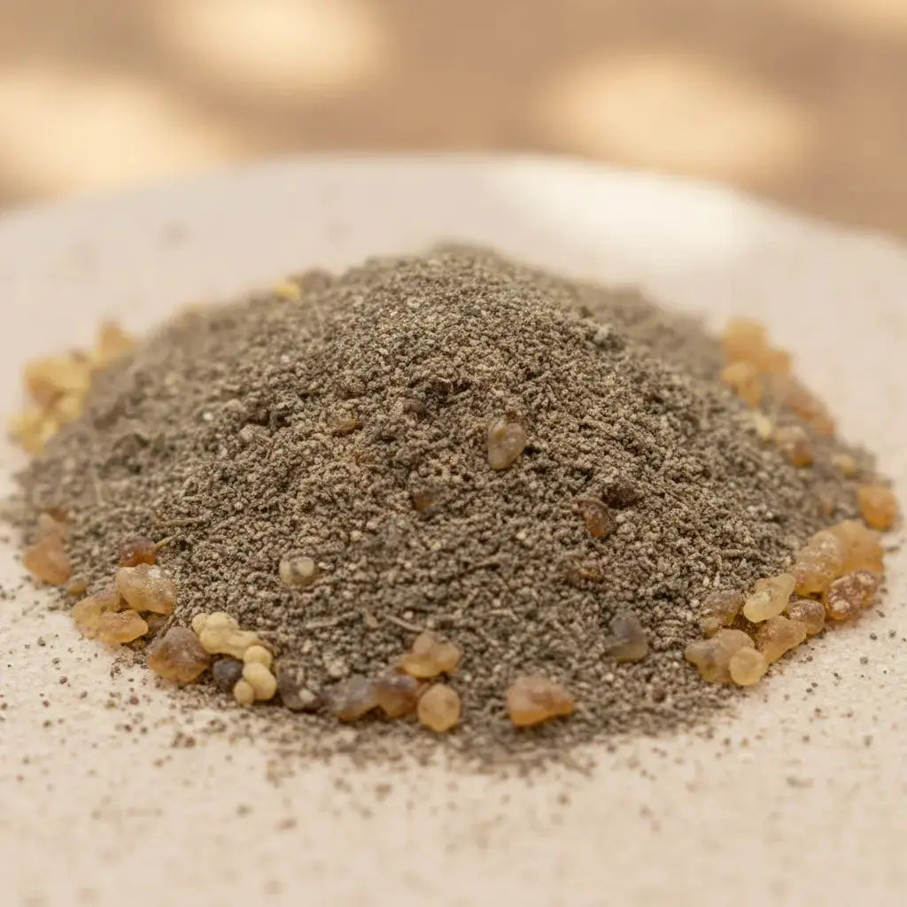 Gros plan sur un tas de poudre d’encens Vénus grisée, parsemée de petits grains de résine dorés sur fond clair.