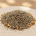 Gros plan sur un tas de poudre d’encens Vénus grisée, parsemée de petits grains de résine dorés sur fond clair.