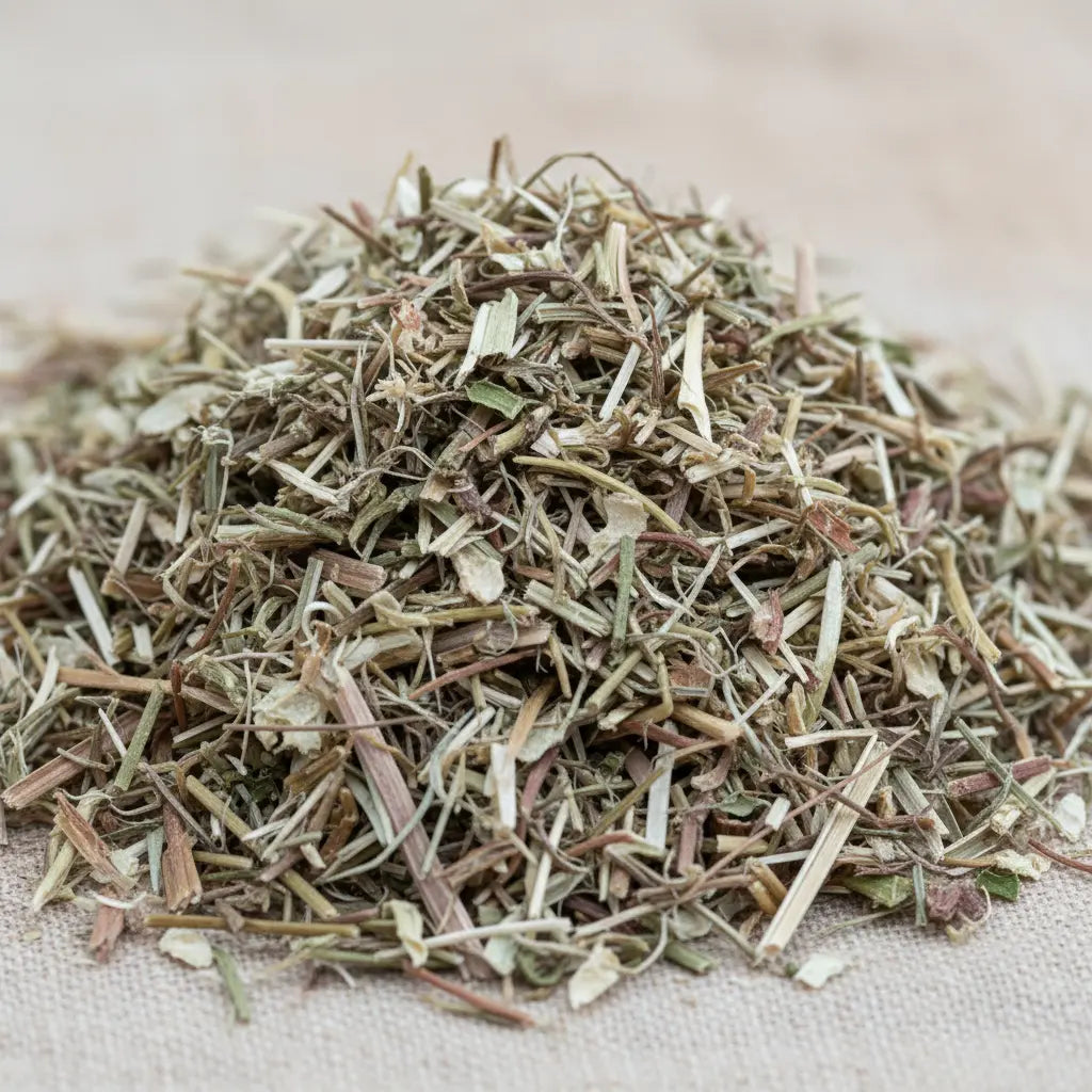 Gros plan sur un petit tas de verveine séchée, composé de fins fragments de tiges et de feuilles vert-brun sur une toile beige.