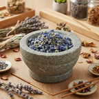 Grains d'encens de résine Vierge Marie (bleu et gris) dans un mortier en granit gris, entouré de brins de lavande, de sauge blanche et de bâtonnets d'encens.