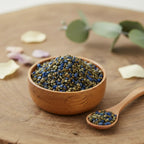 Grains d'encens de résine Vierge Noire, mélange de teintes bleu marine et brun/vert olive, dans un bol en bois sur une tranche de tronc d'arbre, avec cuillère.