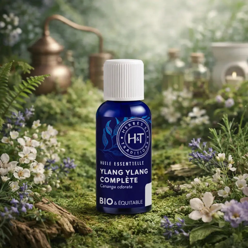 Flacon en verre bleu Herbes et Traditions - Huile Essentielle - Ylang Ylang entouré de petites fleurs blanches et violettes sur un lit de mousse.